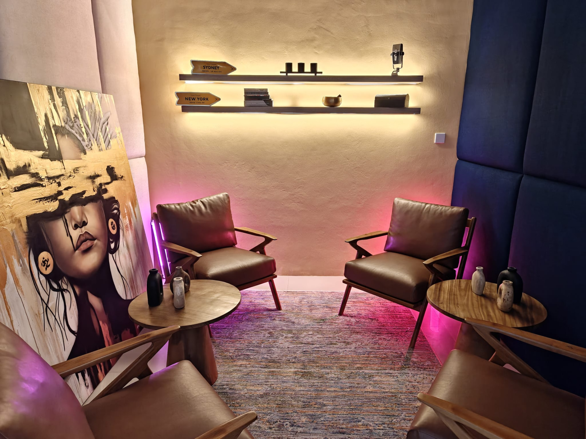 The Great Room — a styled studio with a leaning portrait painting, mid-century armchairs and dramatic pink accent lighting